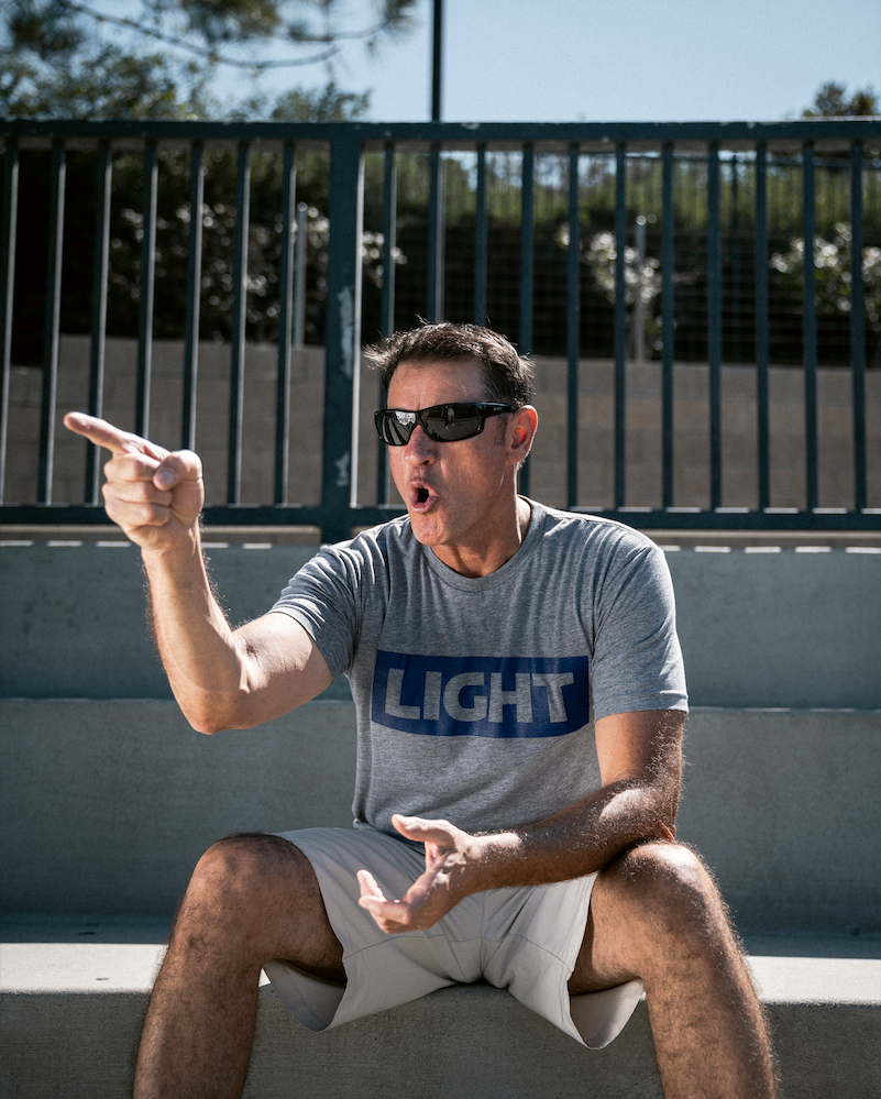 Man sitting on a ledge wearing sunglasses and a gray t-shirt with 'LIGHT' printed on it.