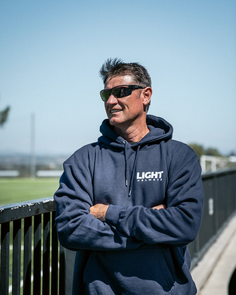 Man wearing a navy hoodie with 'Light' branding, standing outdoors with a clear sky.