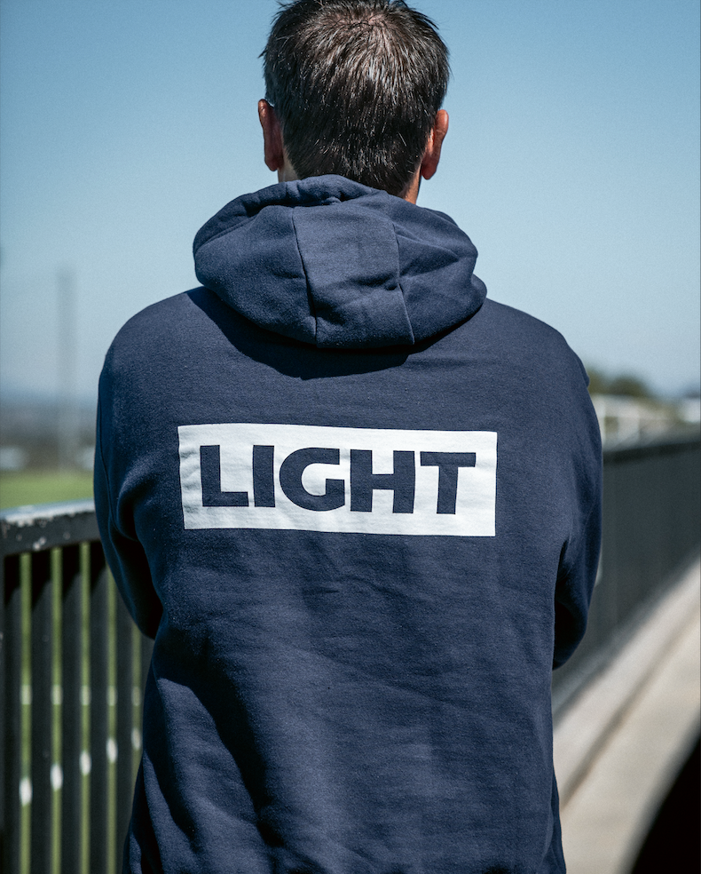 Person wearing a navy hoodie with 'LIGHT' printed on the back, standing outdoors.