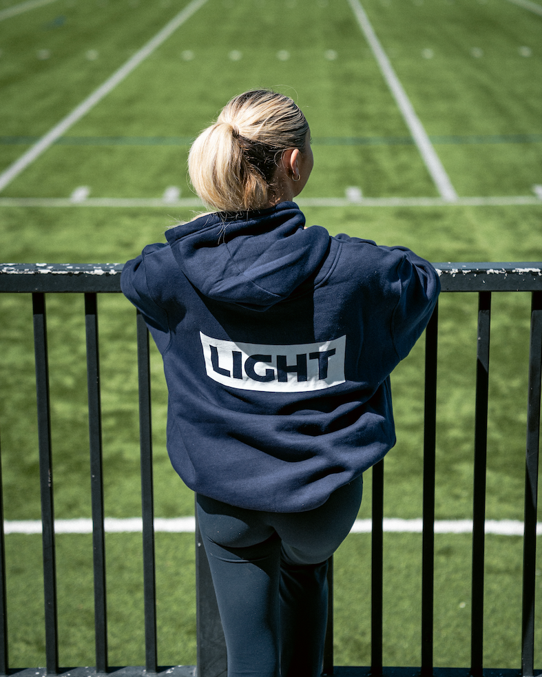 Person wearing a navy hoodie with 'LIGHT' on the back, standing on a football field.