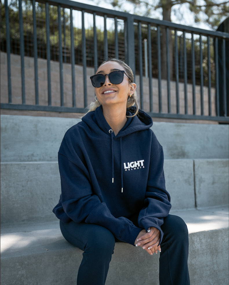 Person wearing a navy hoodie with 'LIGHT' branding sitting on steps outdoors.