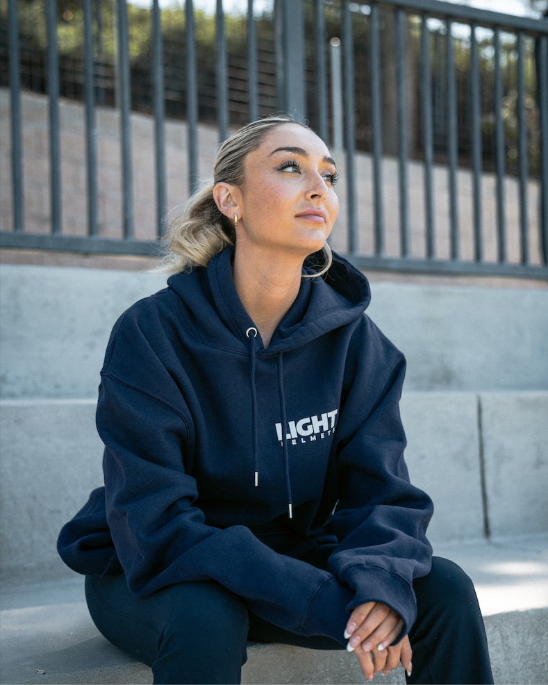 Person wearing a navy hoodie with 'LIGHT' branding sitting on steps.