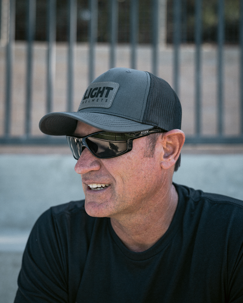 Man wearing a gray cap with 'LIGHT' logo and sunglasses, sitting outdoors.