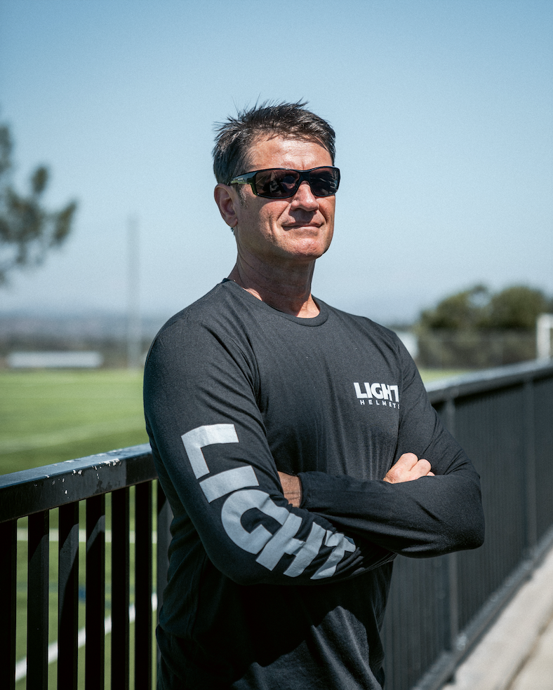 Man wearing sunglasses and a black shirt with 'LIGHT' branding, standing outdoors.