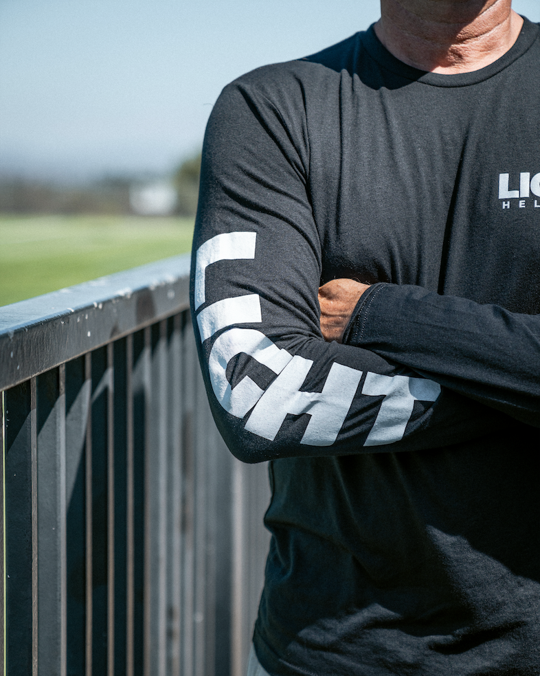 Person wearing a black long-sleeve shirt with white branding on an outdoor setting