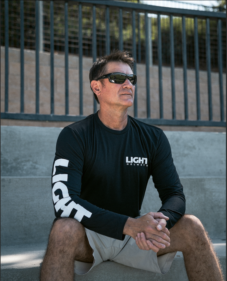 Man wearing a black 'LIGHT' branded long-sleeve shirt sitting on concrete steps.