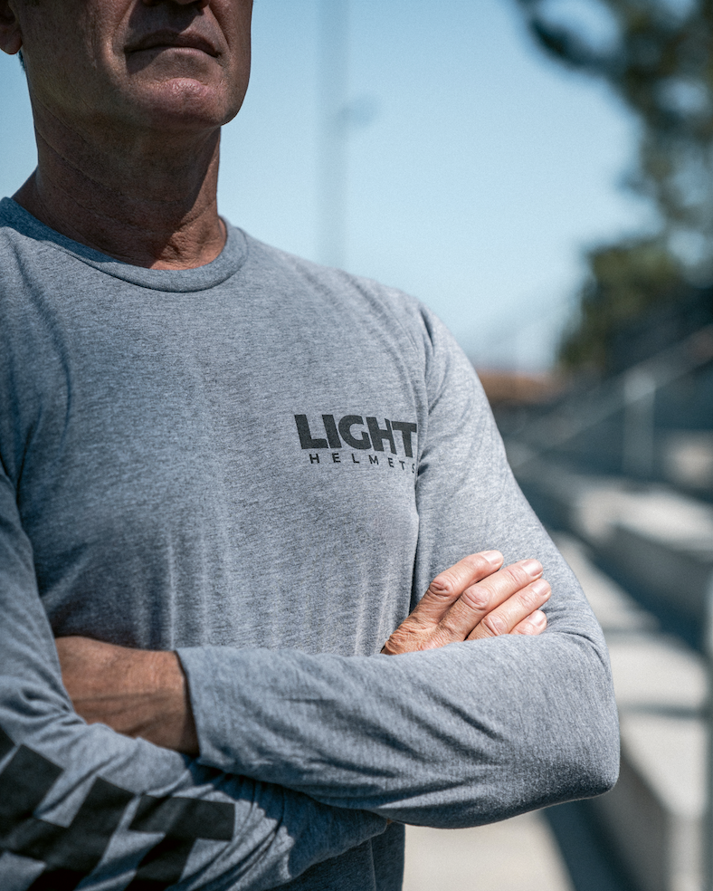 Man wearing a gray long-sleeve shirt with 'LIGHT HELMETS' logo, standing outdoors.