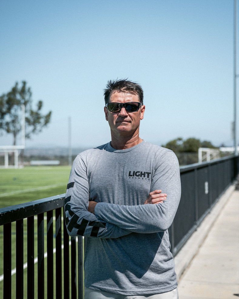 Man wearing sunglasses and a gray long-sleeve shirt with 'LIGHT' branding, standing outdoors.