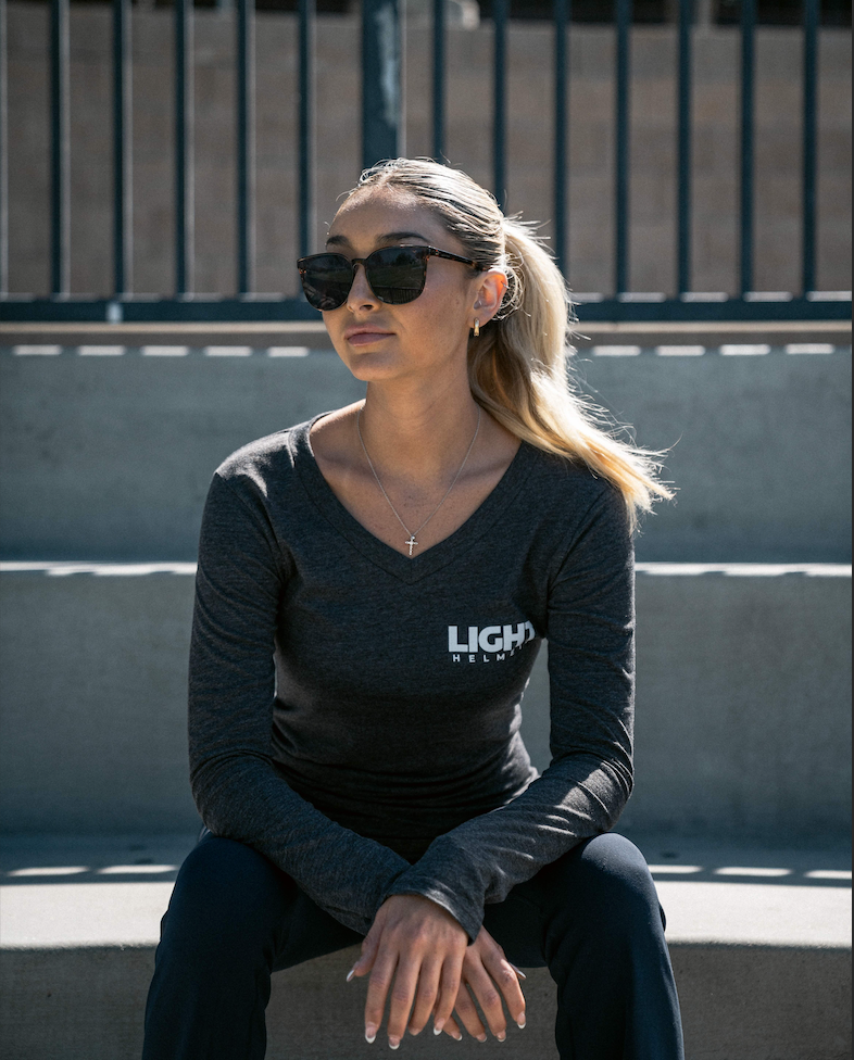 Woman wearing sunglasses and a dark long-sleeve shirt with 'LIGHT' logo sitting on a bench.
