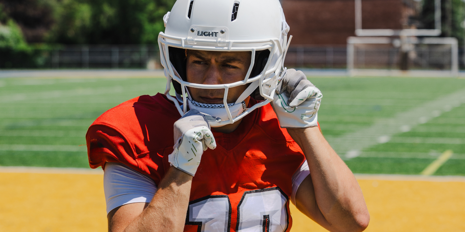 Football player wearing a LIGHT Gladiator matte white football helmet on a football field