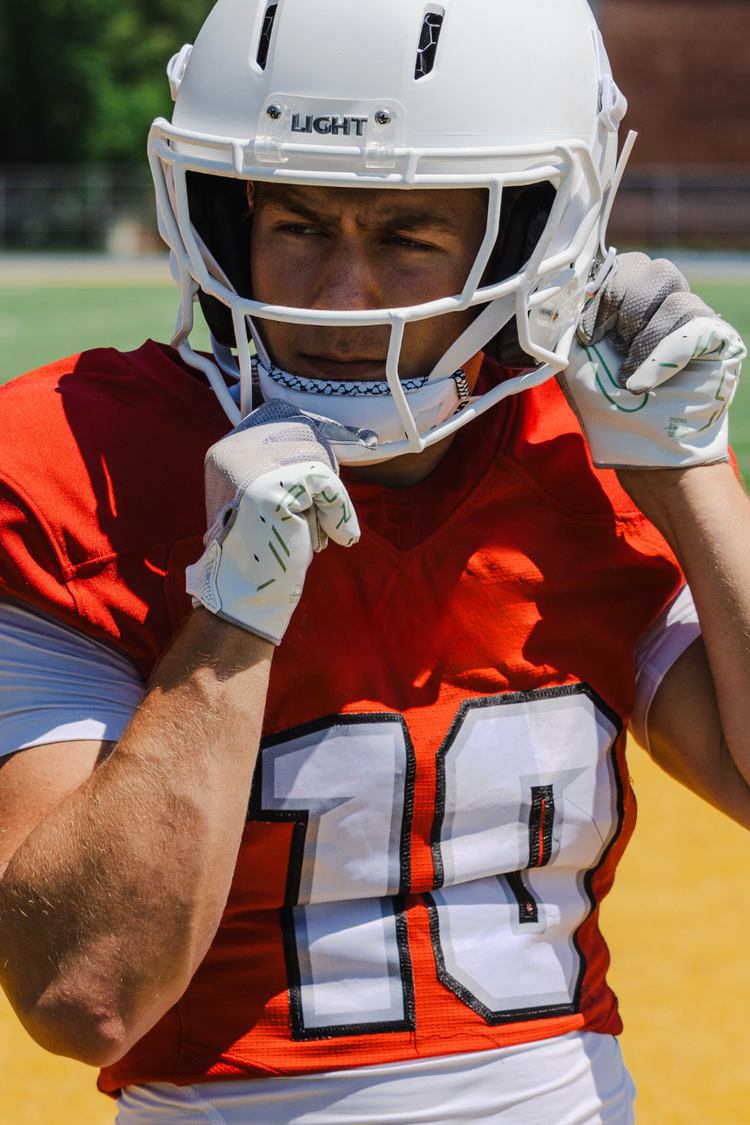 Football player wearing a LIGHT Gladiator matte white football helmet on a football field