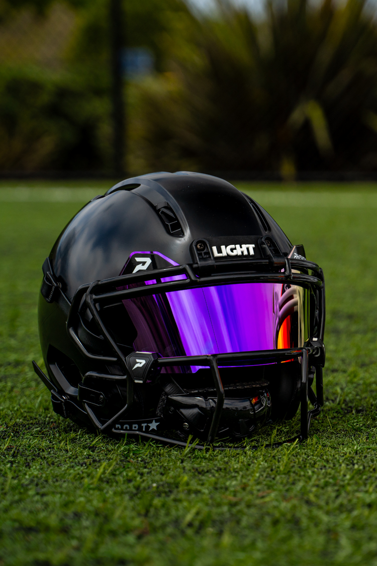 Black Gladiator ATK football helmet sitting on a football field with a purple Phenom visor