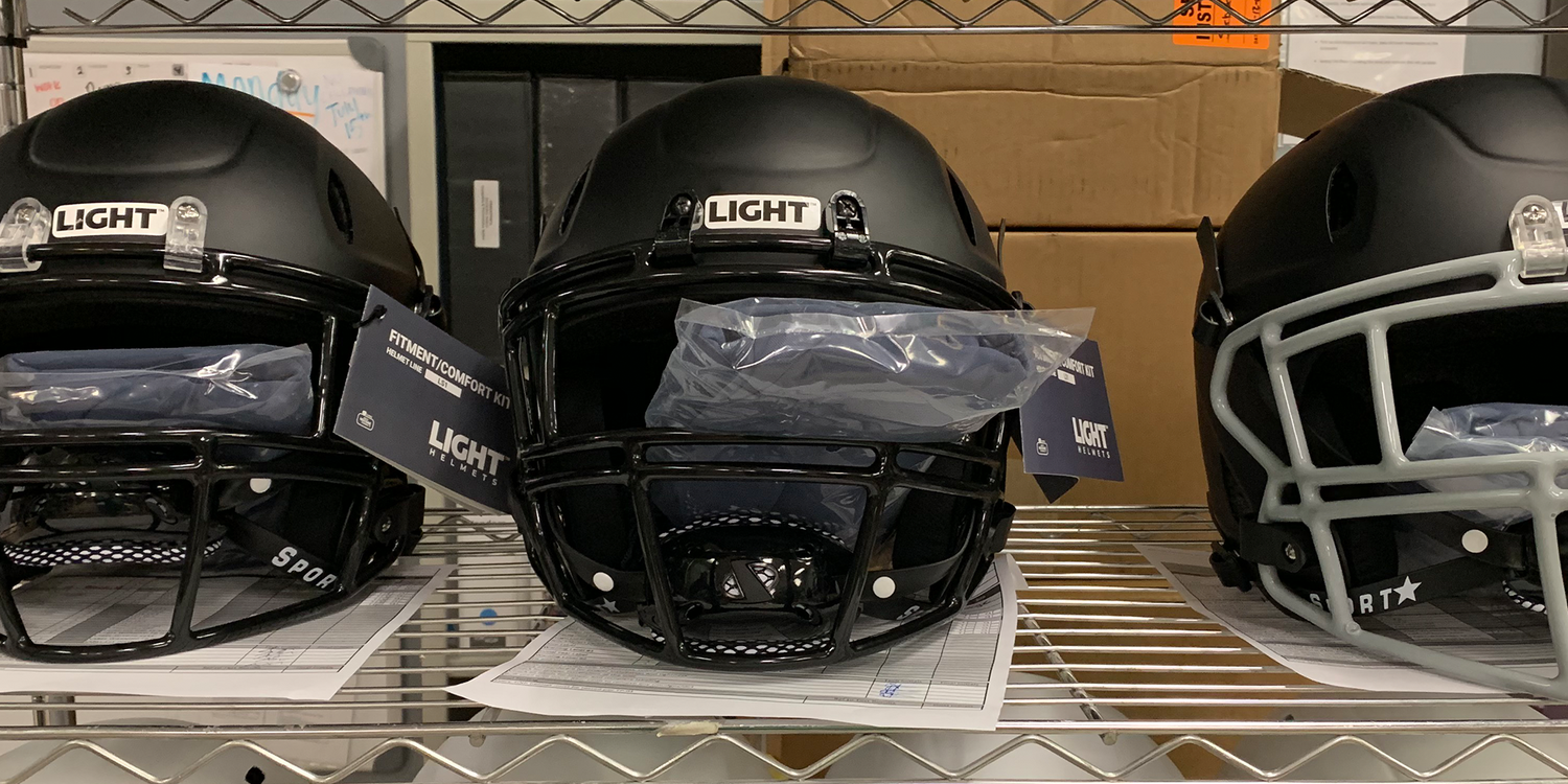 Three Matte Black LIGHT LS2 Composite Varsity Football Helmets on a shelf ready to be reconditioned