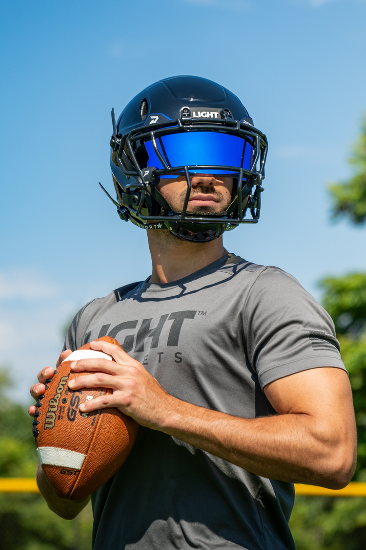 Football player wearing a LIGHT LS2 football helmet while holding a football on a football field